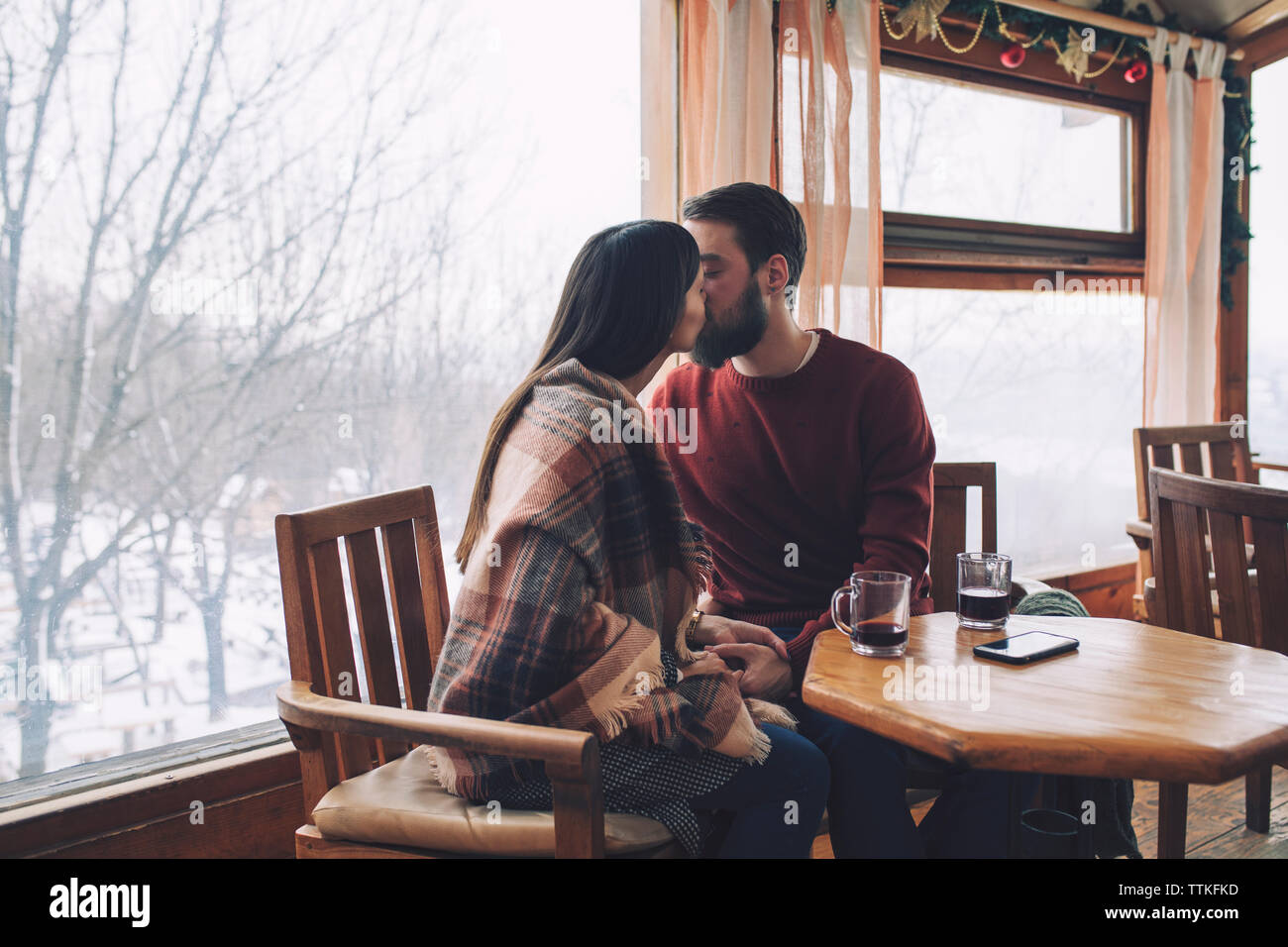 Junges Paar küssen beim Sitzen im Cafe im Winter Stockfoto