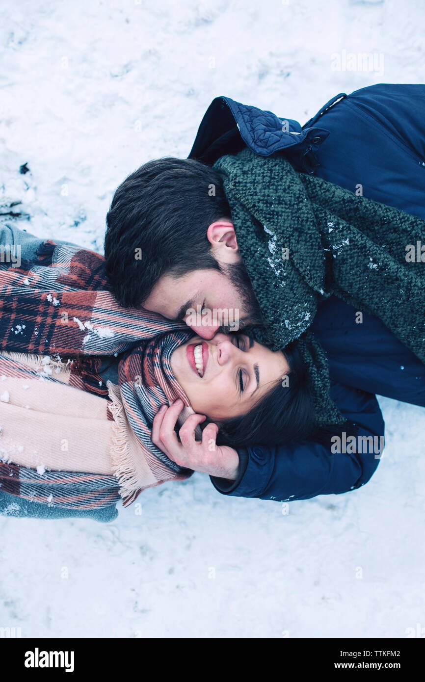 Hohe Betrachtungswinkel des Menschen küssen Freundin beim Liegen auf schneebedeckten Feld Stockfoto