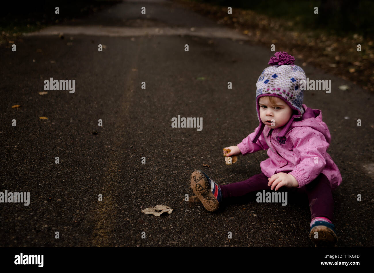 Kleines Mädchen sitzen auf Pathway holding Laub im Herbst Stockfoto