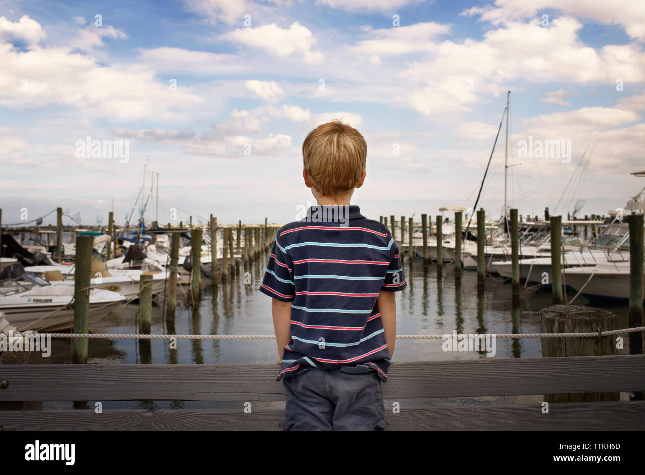 Rückansicht der Junge auf der Brücke von Hafen gegen bewölkter Himmel Stockfoto