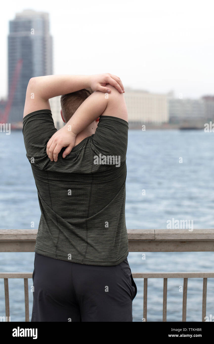 Rückansicht der übergewichtigen Mann stretching Arme hinter zurück beim Stehen auf der Brücke über den Fluss in die Stadt Stockfoto
