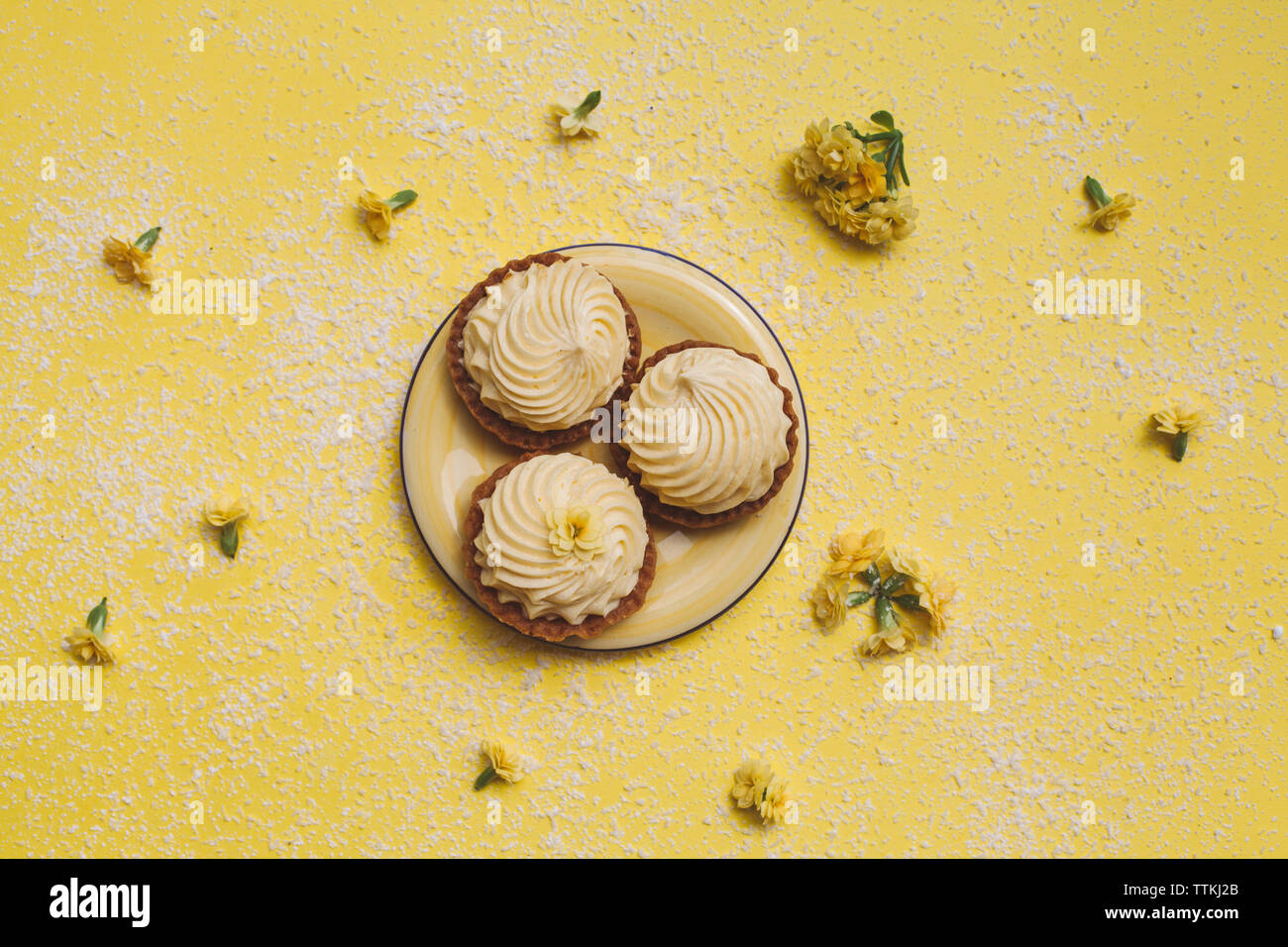 Ansicht von oben von Cupcakes in der Platte mit Blumen auf gelbem Hintergrund Stockfoto