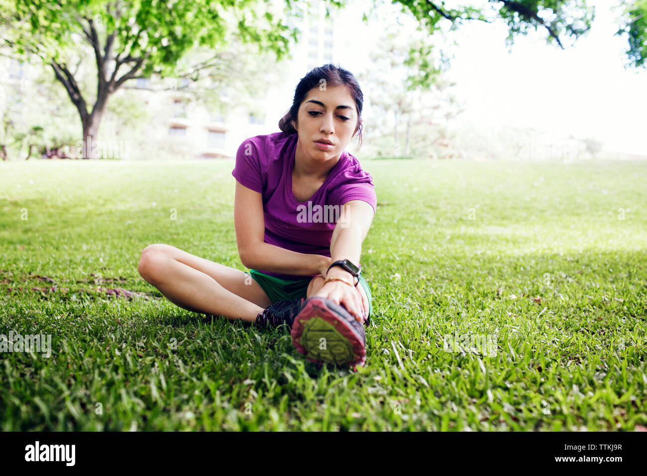 Bestimmt weiblichen Athleten berühren Zehen, während auf dem Rasen im Park sitzen Stockfoto