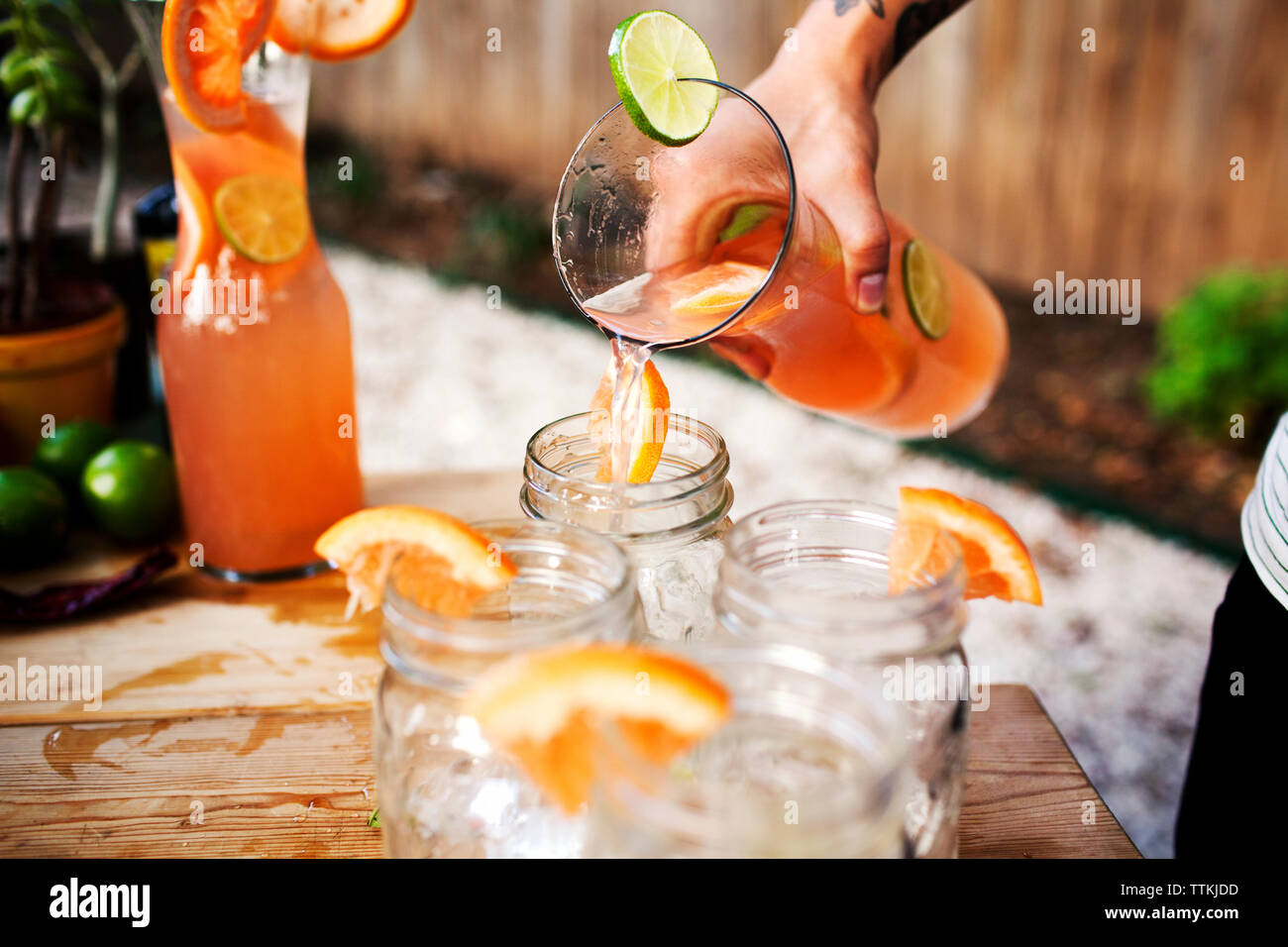 Zugeschnittenes Bild des Menschen gießen Getränk im Glas auf dem Tisch Stockfoto