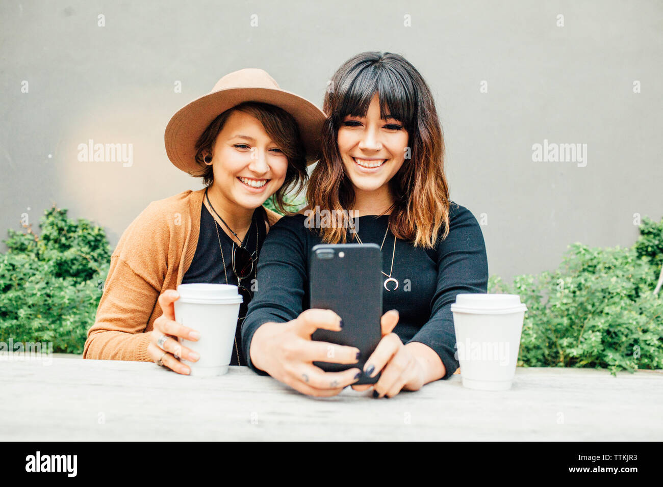 Weibliche Freunde unter selfie beim Sitzen am Tisch gegen die Wand Stockfoto