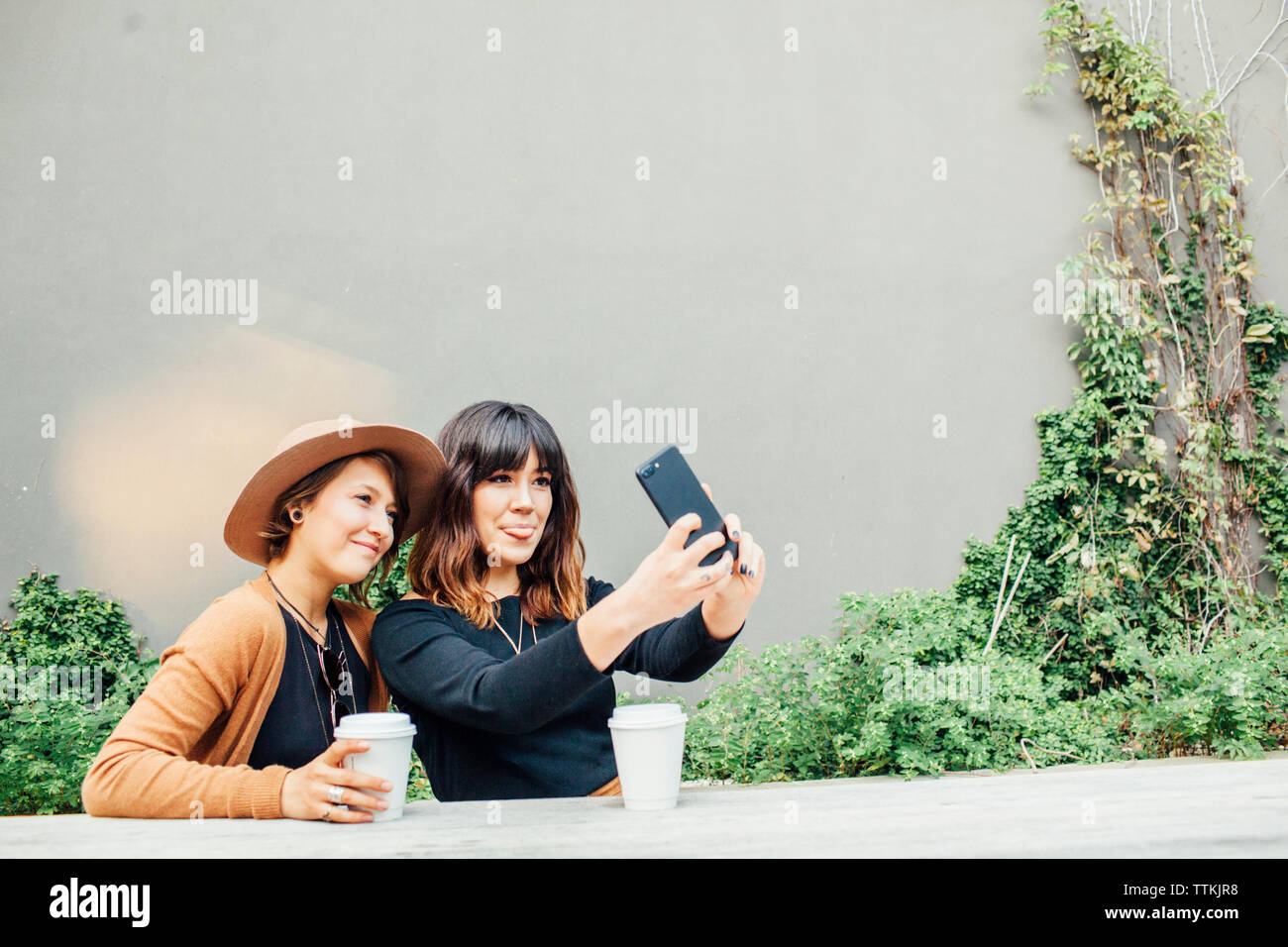 Junge weibliche Freunde unter selfie beim Sitzen am Tisch gegen die Wand Stockfoto