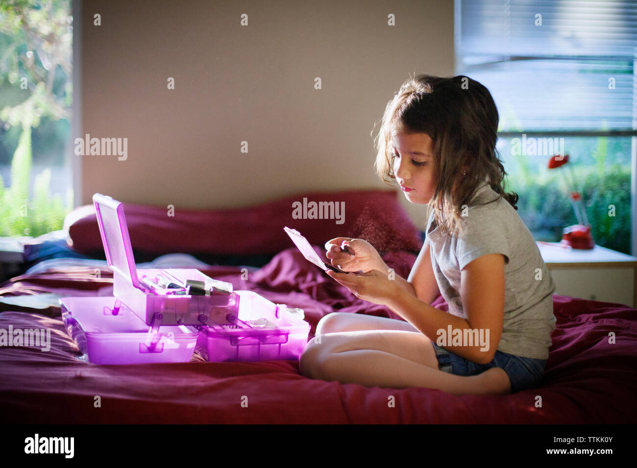 Seitliche Sicht auf Mädchen sitzen und Anwendung von Make-up im Bett Stockfoto