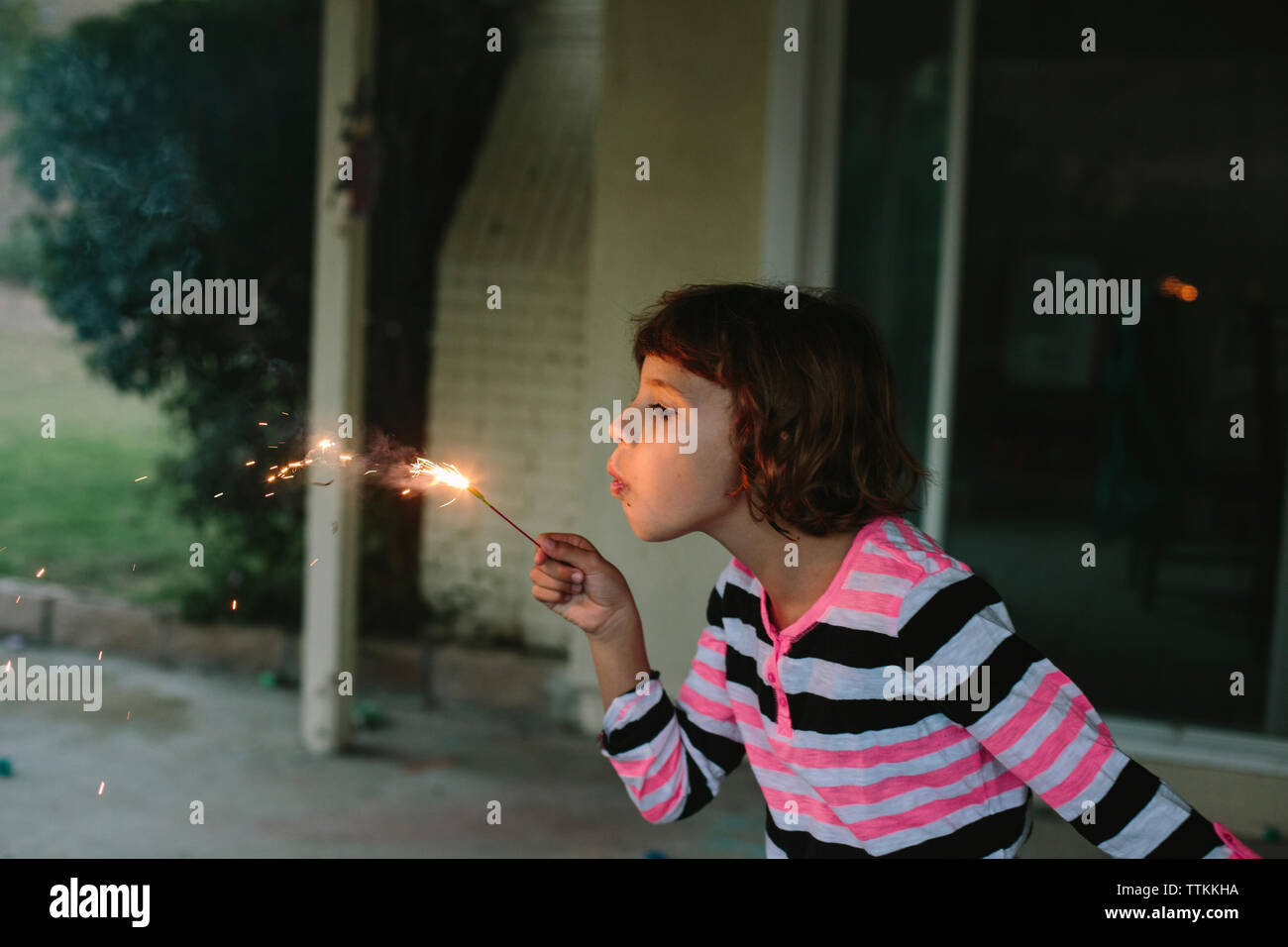 Mädchen bläst brennende Wunderkerze beim Spielen im Hinterhof Stockfoto