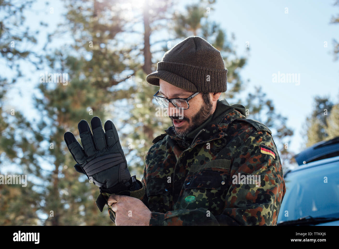 Man Handschuhe tragen, während sich gegen Himmel im Wald Stockfoto
