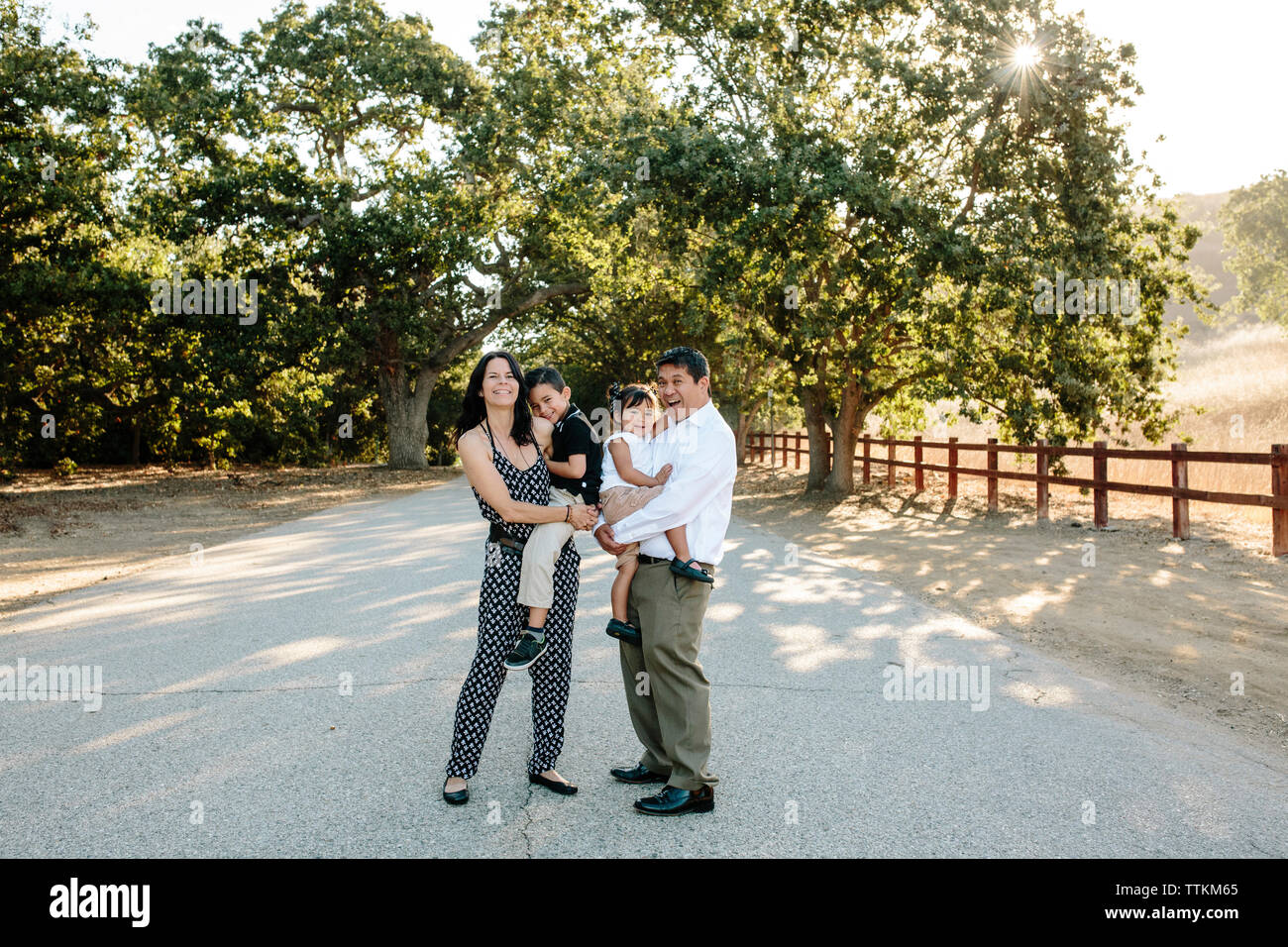 Portrait von glücklichen Eltern Kinder tragen beim Stehen auf Straße gegen Bäume im Park Stockfoto