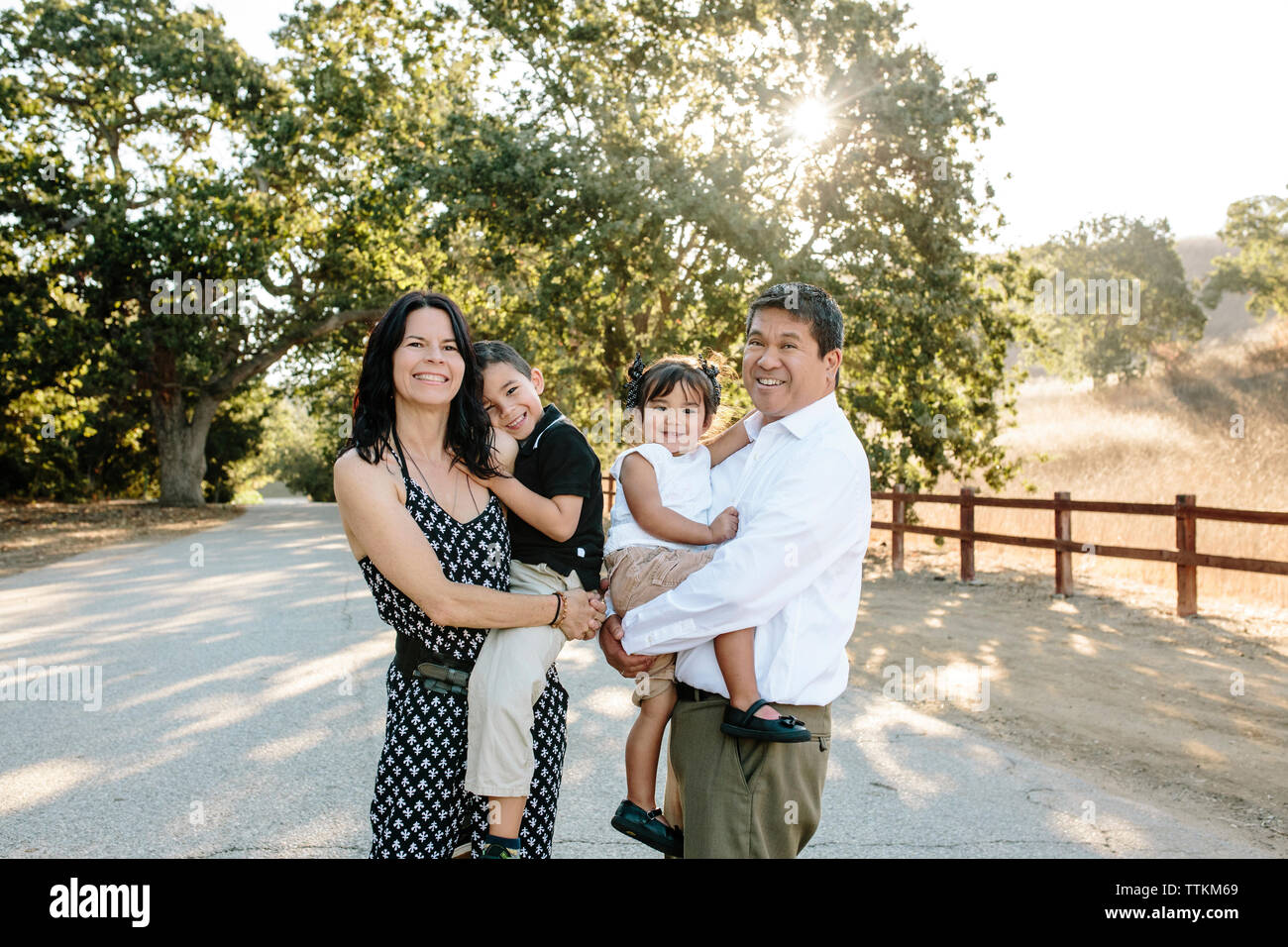Portrait von glücklichen Eltern mit niedlichen Kinder beim Stehen auf Straße gegen Bäume im Park Stockfoto