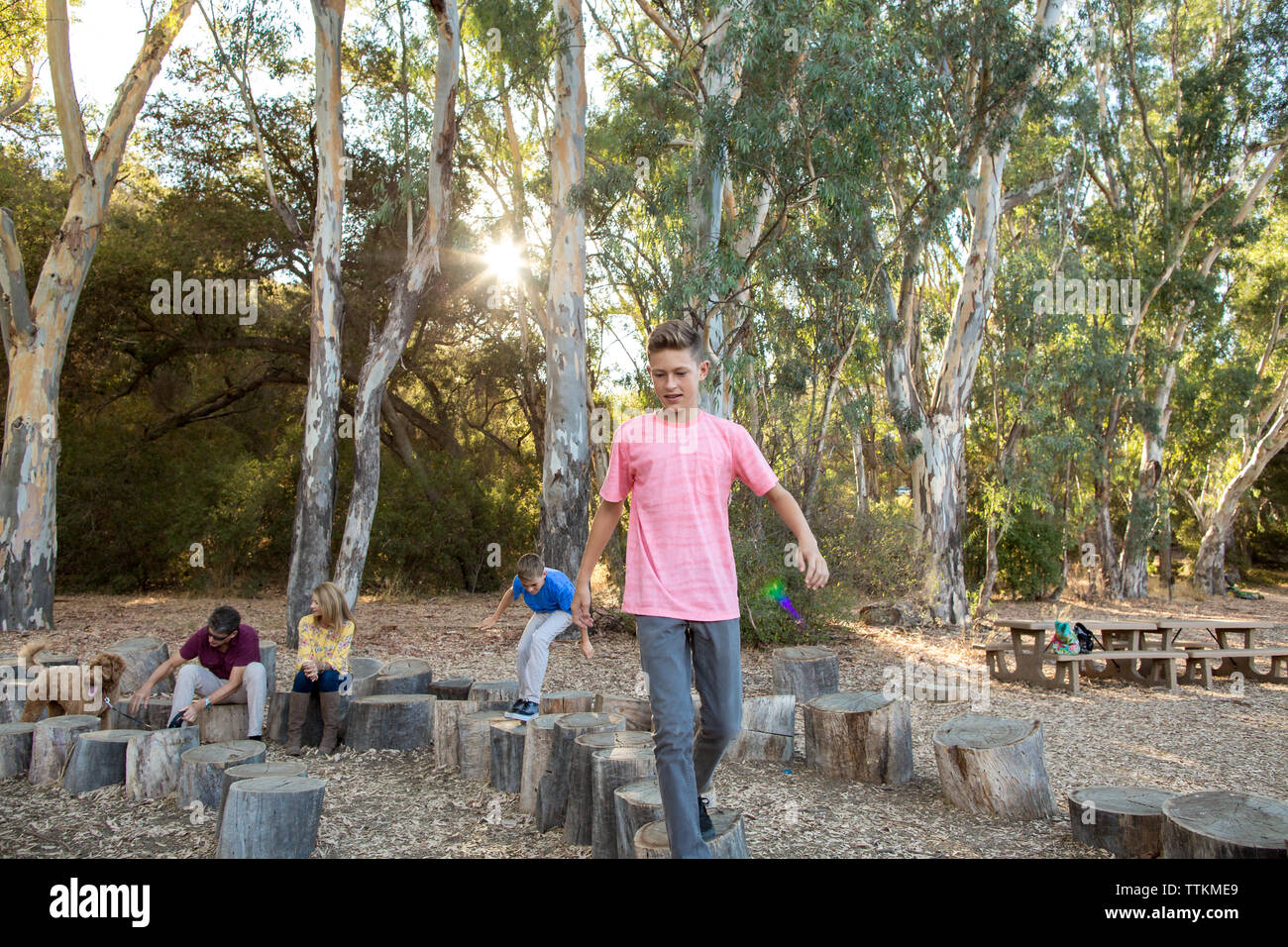Teenager Spaziergänge auf Baumstümpfen mit Sun flare und Familie hinter Stockfoto
