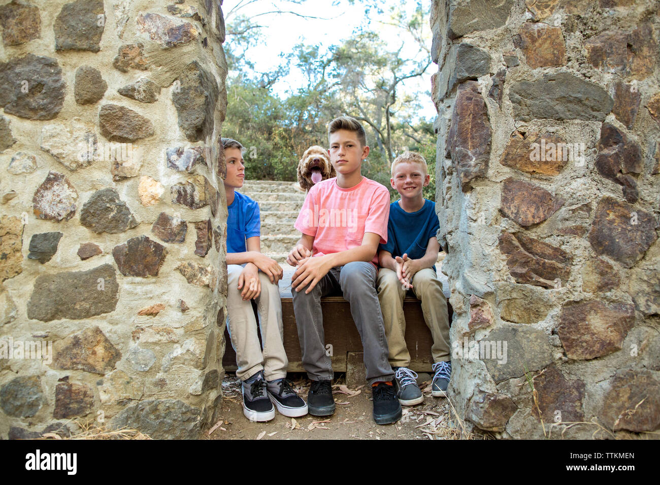 Drei Brüder sitzen innerhalb einer Steinmauer Rahmen mit Hund hinter Ihnen Stockfoto