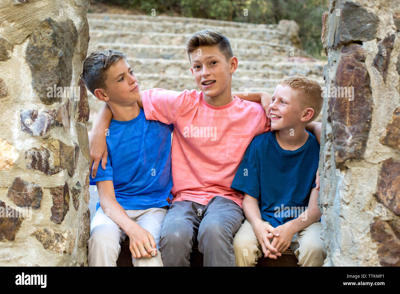 Zwei jüngere Brüder Blick auf ältere Bruder beim Sitzen durch Steinmauer Stockfoto