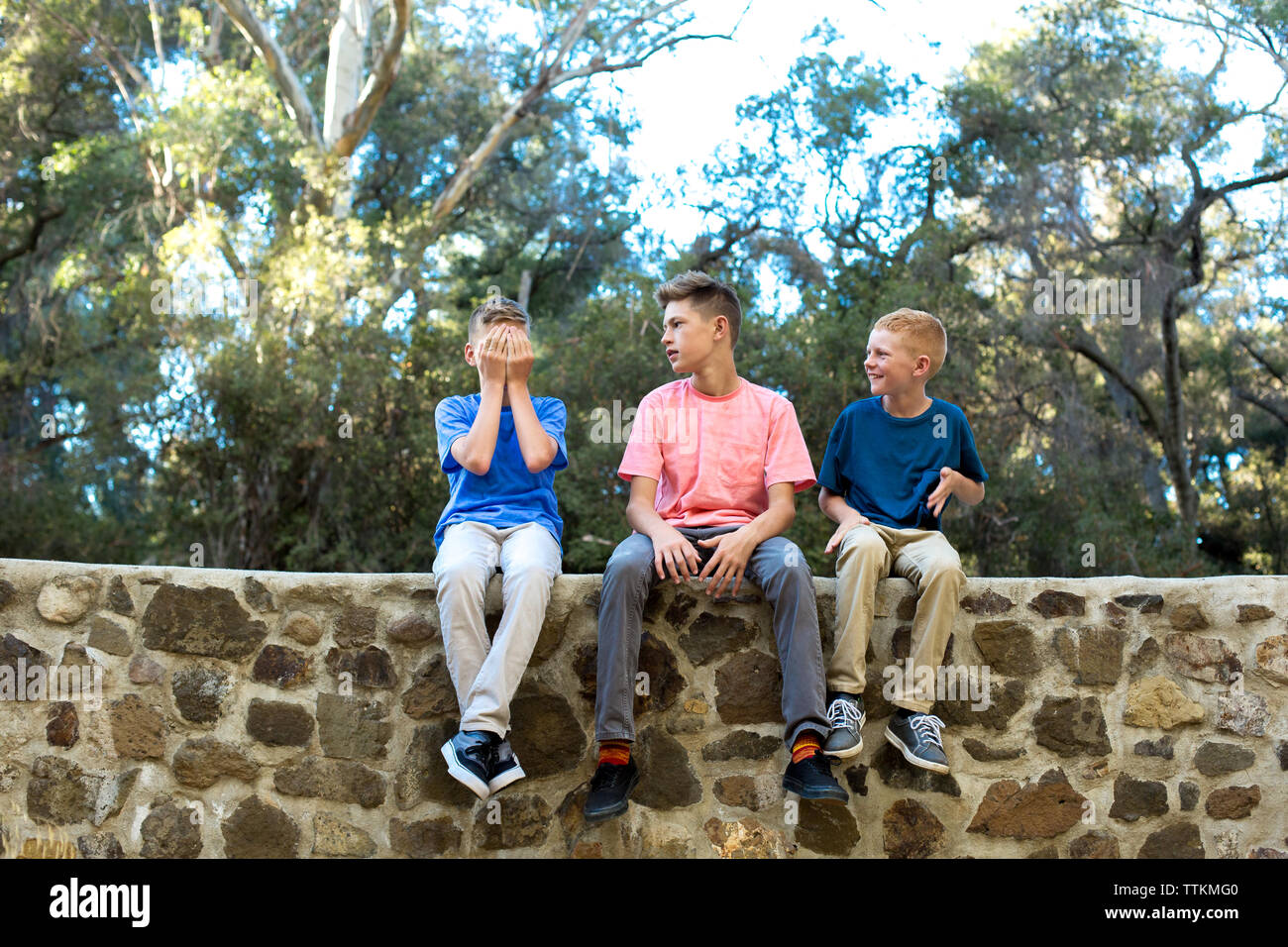 Drei Jungs sitzen auf einer Wand, während ein Bruder deckt Gesicht Stockfoto