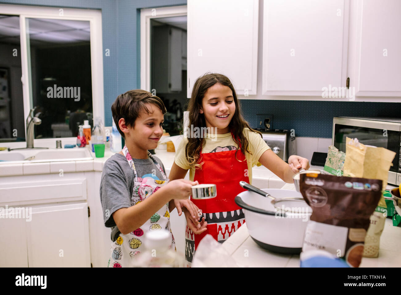 Bruder und Schwester Lächeln beim Backen in der Küche bei Nacht Stockfoto