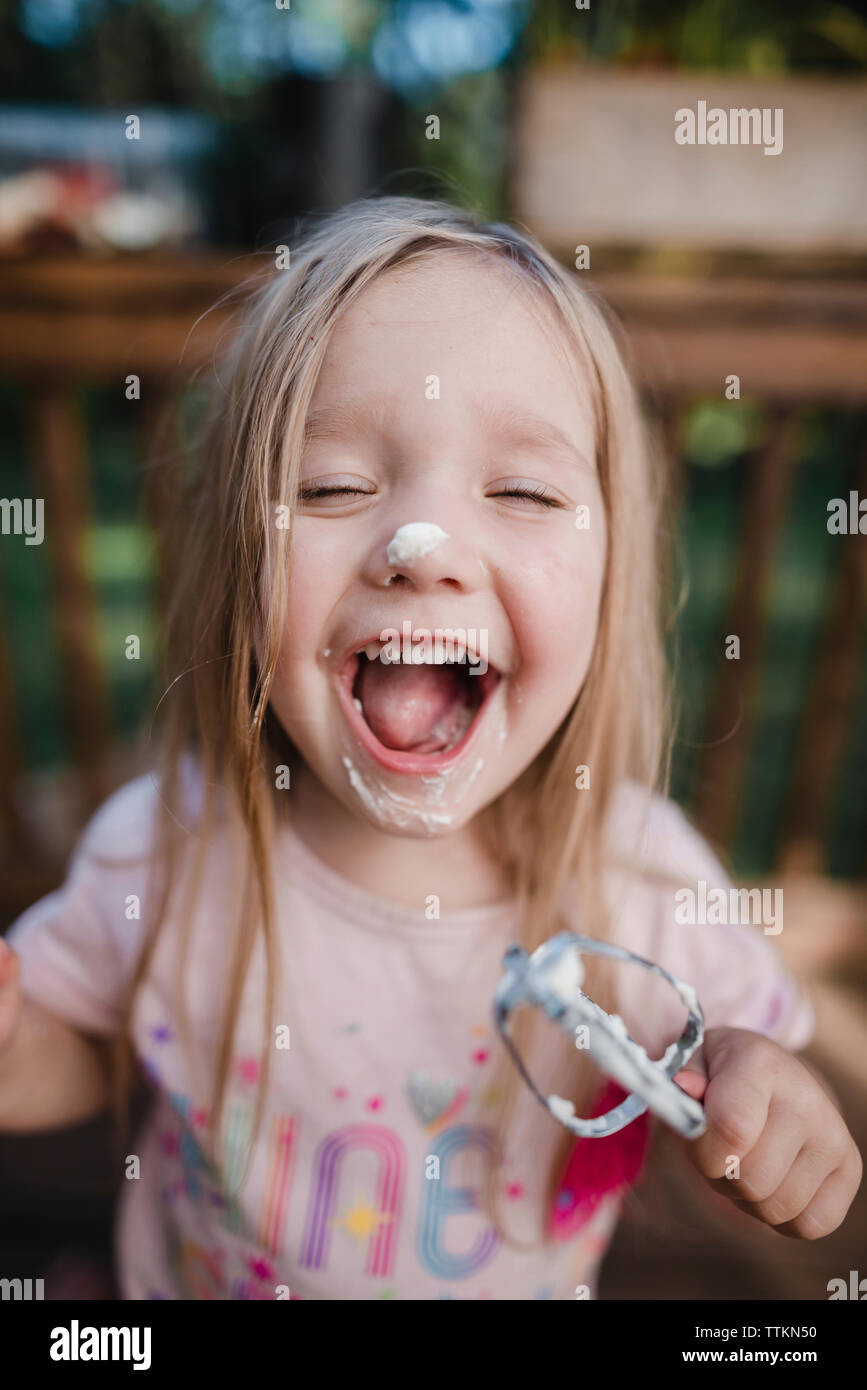 Verspielte Mädchen mit geschlossenen Augen lachen, während sie Schneebesen Stockfoto