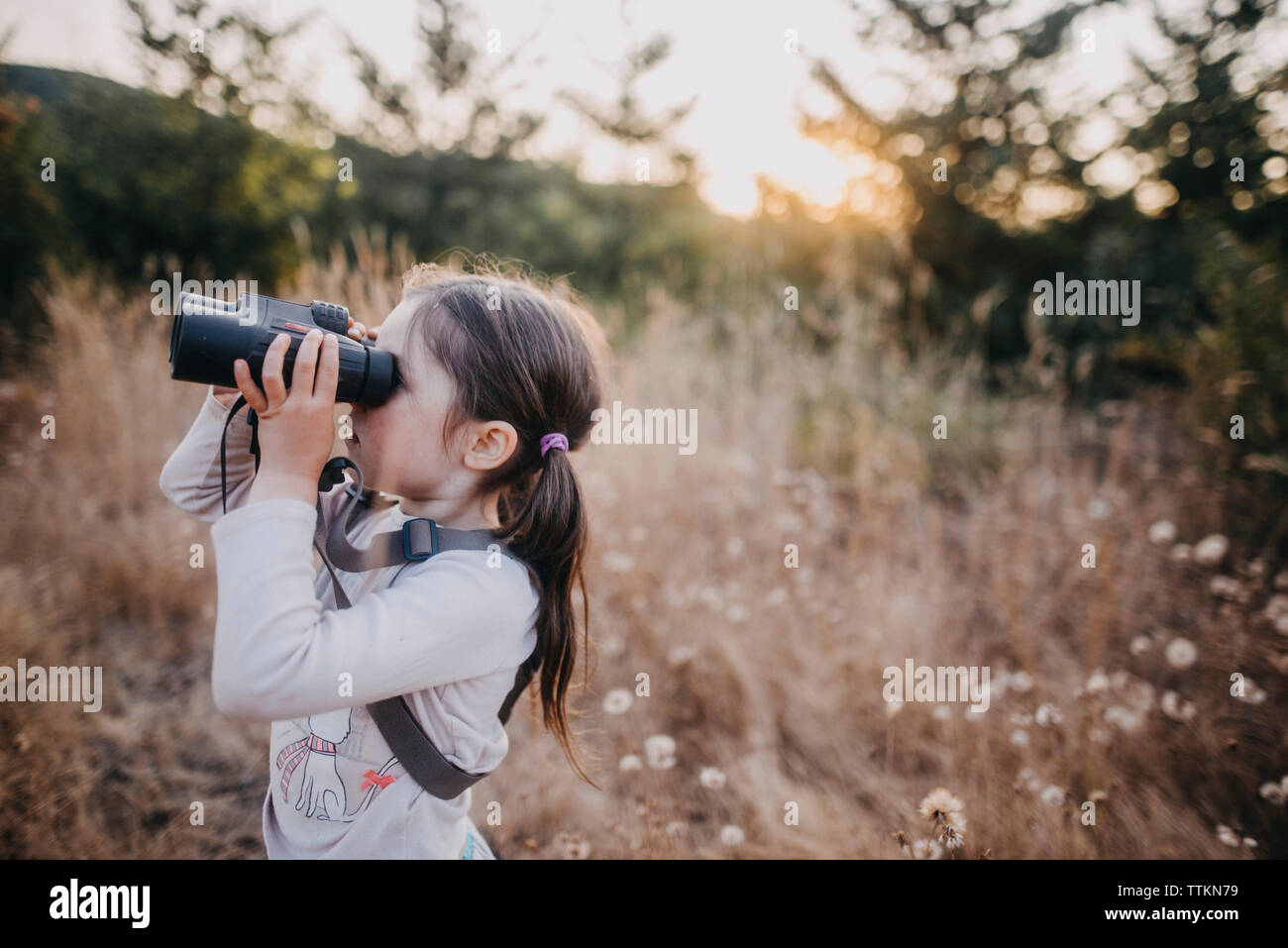 Seitenansicht des Mädchens auf der Suche durchs Fernglas beim Stehen auf Feld Stockfoto