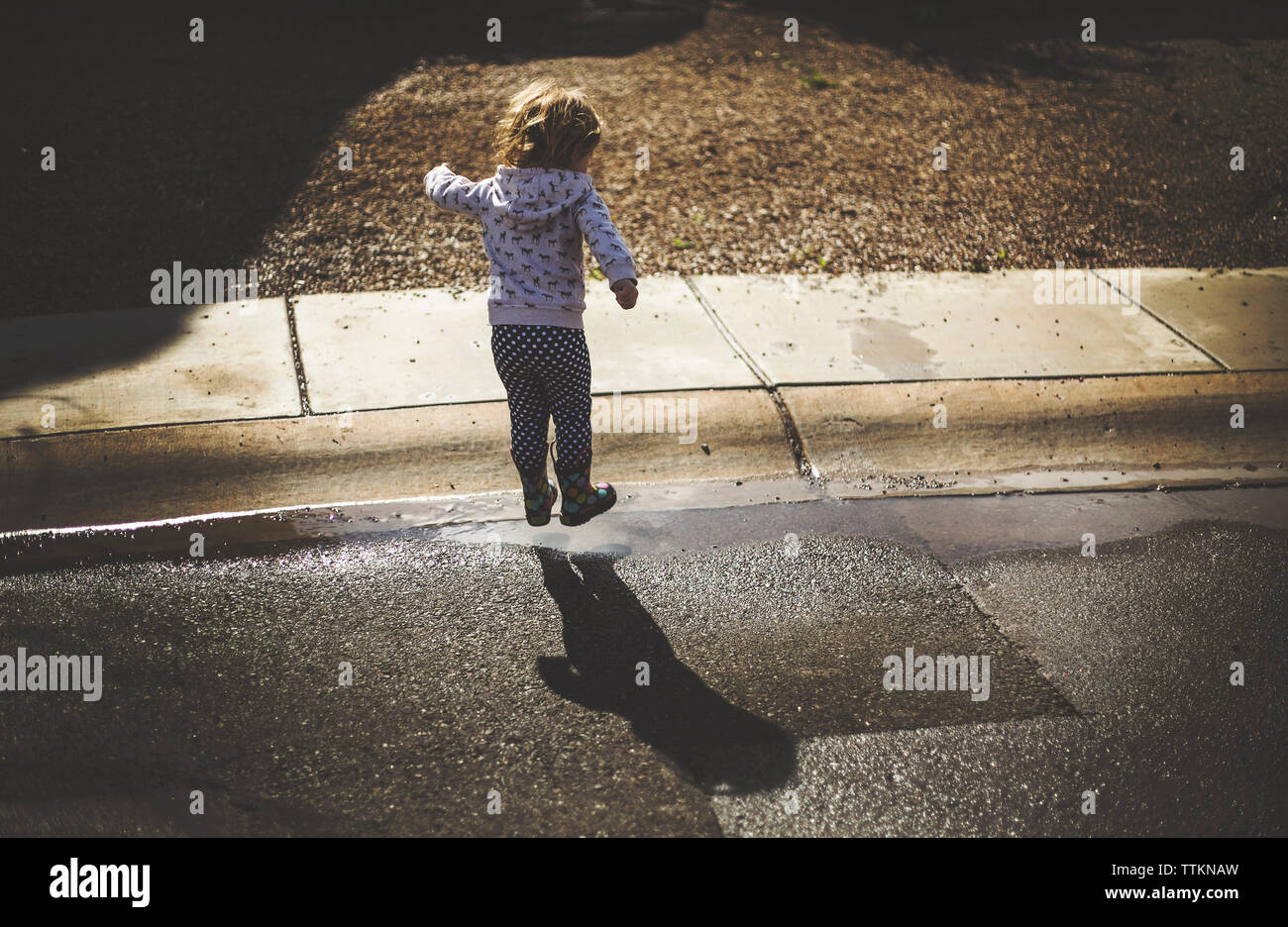 Ansicht der Rückseite des Mädchen spielen auf nasser Straße an einem sonnigen Tag Stockfoto