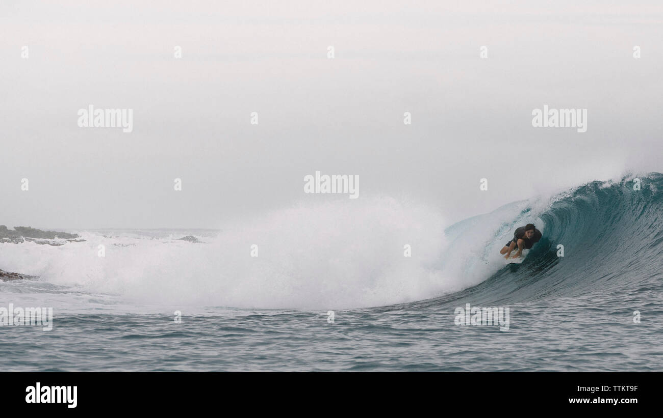 Sorgloser junger Mann surfen auf Rolling Surf im Meer gegen Sky Stockfoto