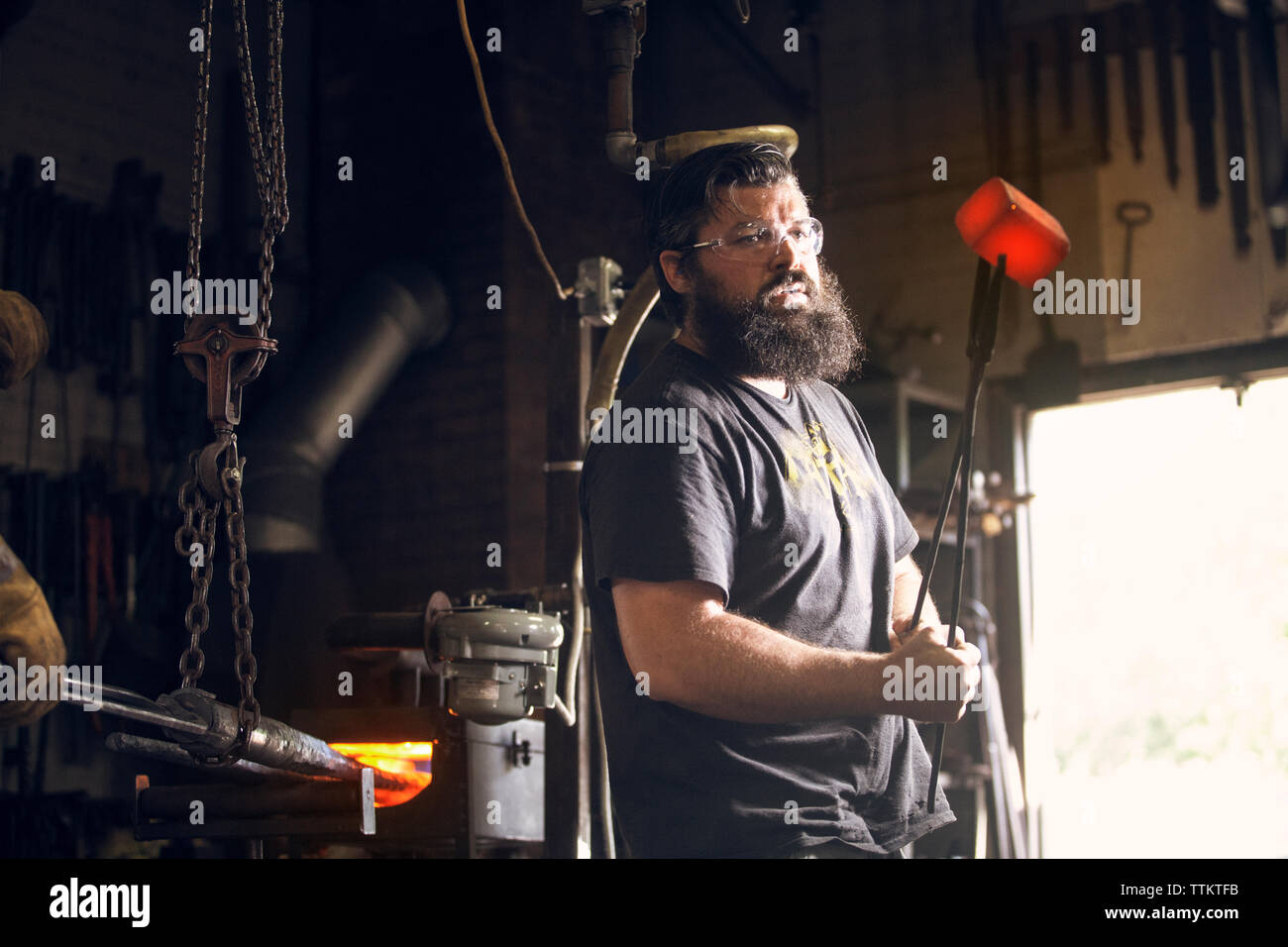 Schmied holding red hot Metal mit Zangen in Werkstatt Stockfoto