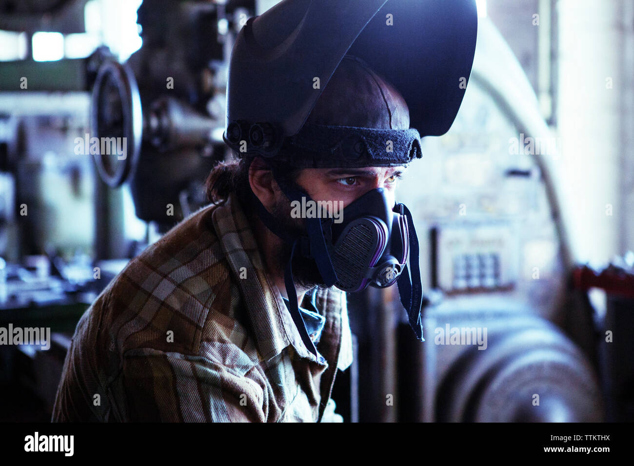 Arbeiter in Arbeitsschutzkleidung, der wegschaut, während er in der Werkstatt sitzt Stockfoto