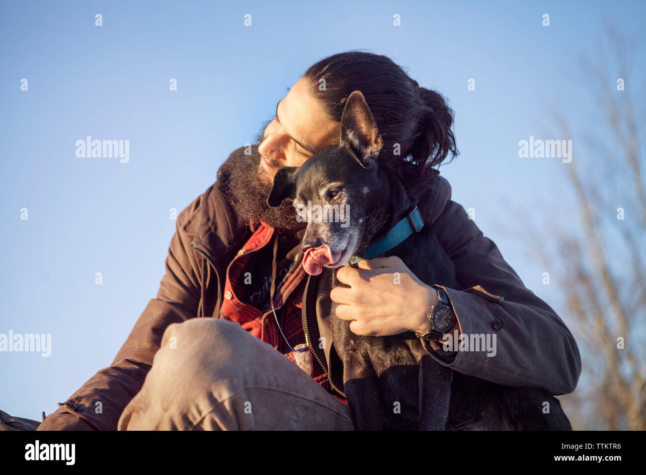 Liebevollen Mann mit Hund, während gegen den klaren blauen Himmel sitzen Stockfoto