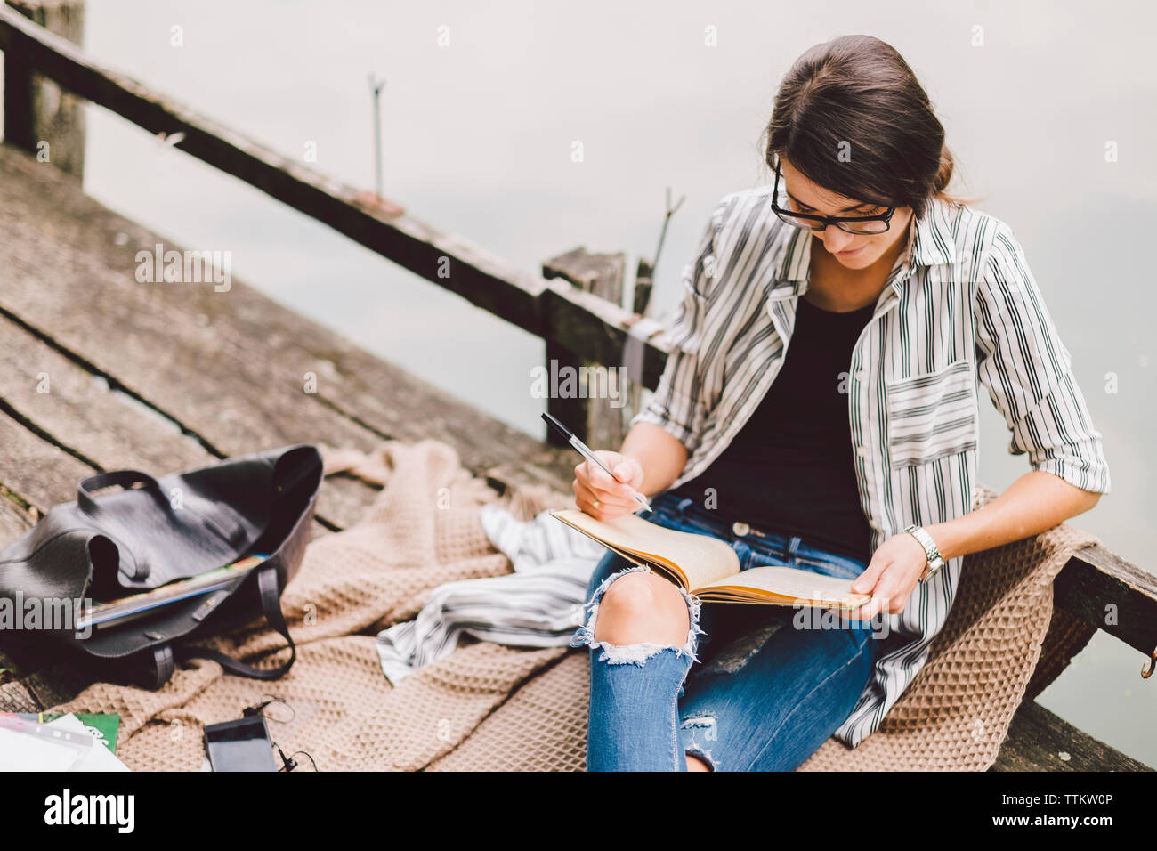 Hohe Betrachtungswinkel von Frau mit Buch beim Sitzen auf Pier gegen See im Wald Stockfoto
