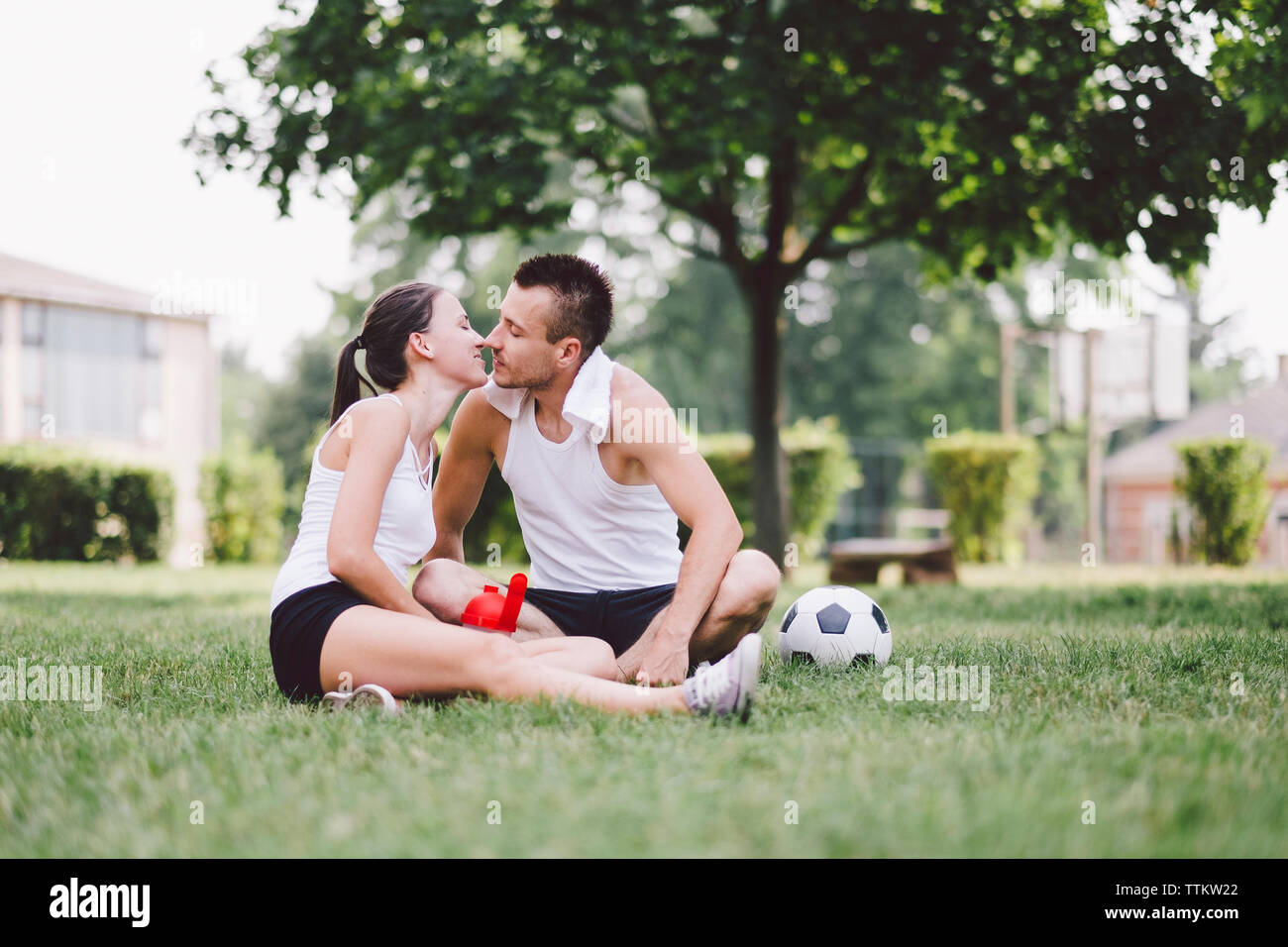 Junges Paar küssen beim Sitzen auf Fußball im Park Stockfoto