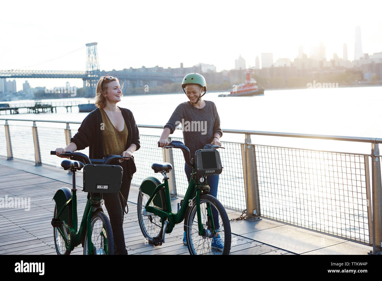 Lächelnd Freunde mit dem Fahrrad zu Fuß über die Promenade am Fluss Stockfoto