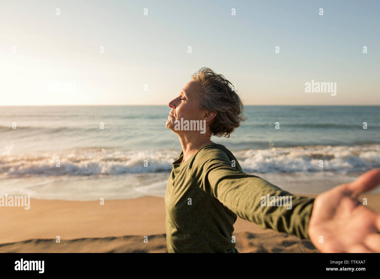 Seitenansicht der Frau mit ausgestreckten Armen am Strand gegen den klaren Himmel Stockfoto
