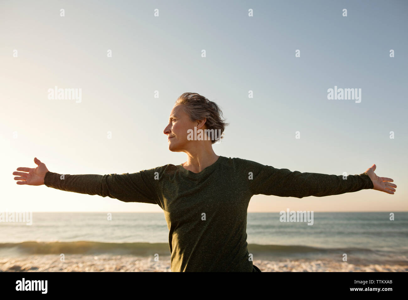 Vorderansicht der Frau mit ausgestreckten Armen am Strand gegen den klaren Himmel Stockfoto