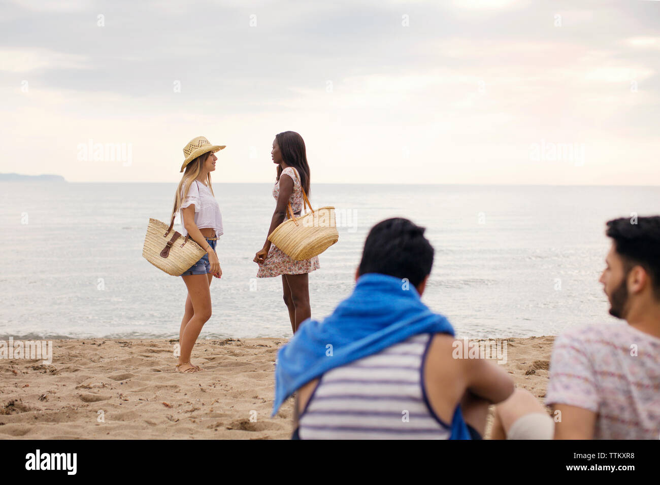 Männliche Freunde auf Frauen stehen auf Ufer am Strand Stockfoto