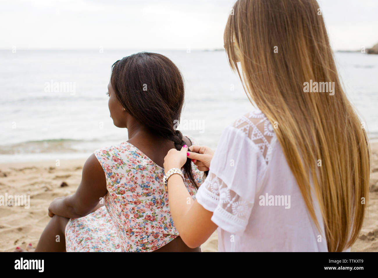 Ansicht der Rückseite Frau Flechten des Freundes Haar, während am Ufer am Strand sitzen Stockfoto