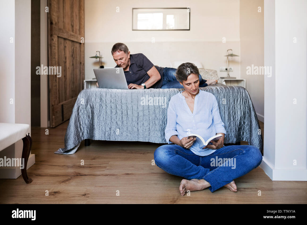 Senior Paar mit Laptop und lesen Buch im Schlafzimmer Stockfoto