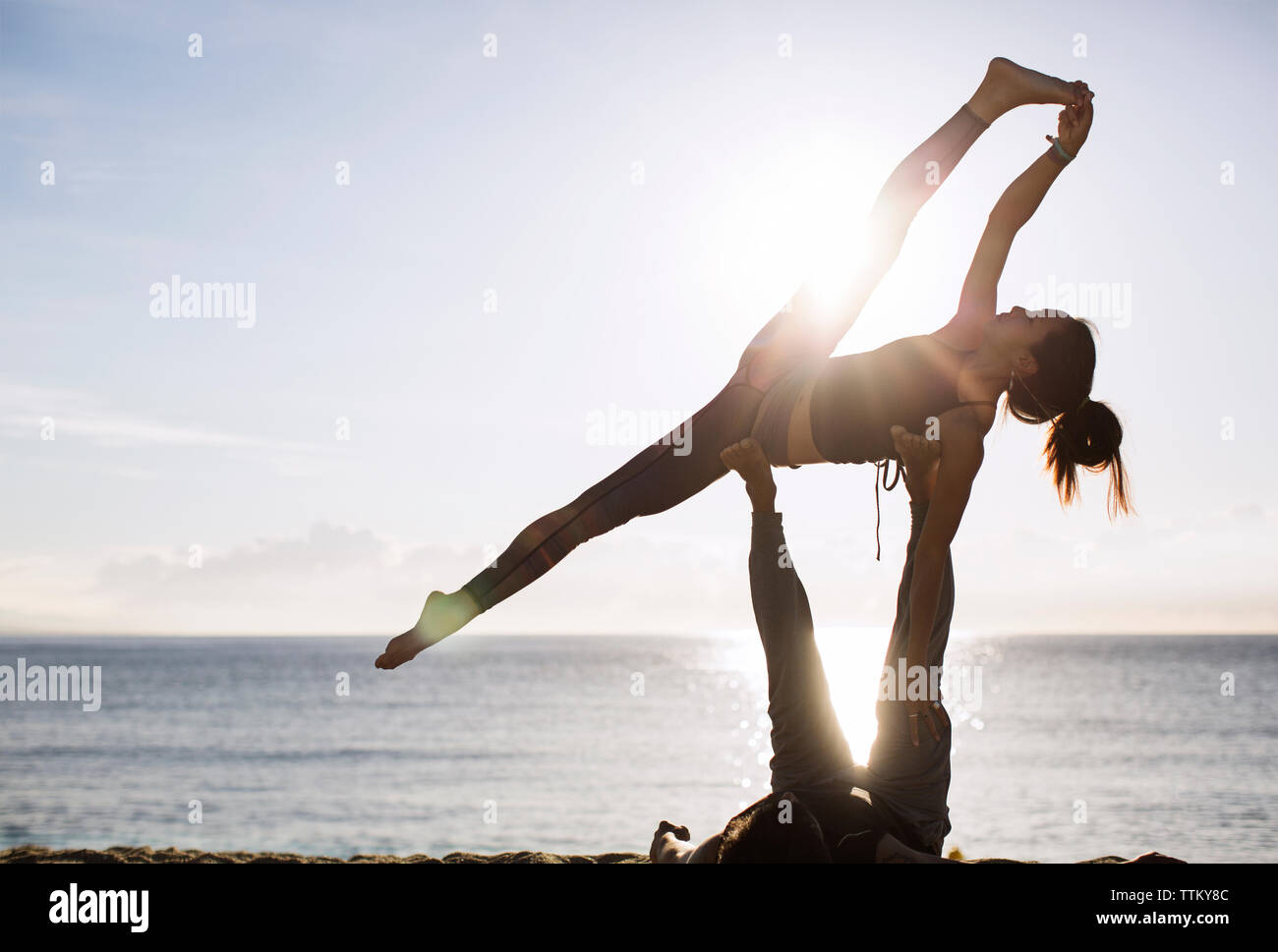 Mann anheben Frau bei der Durchführung von Yoga am Strand gegen Sky Stockfoto