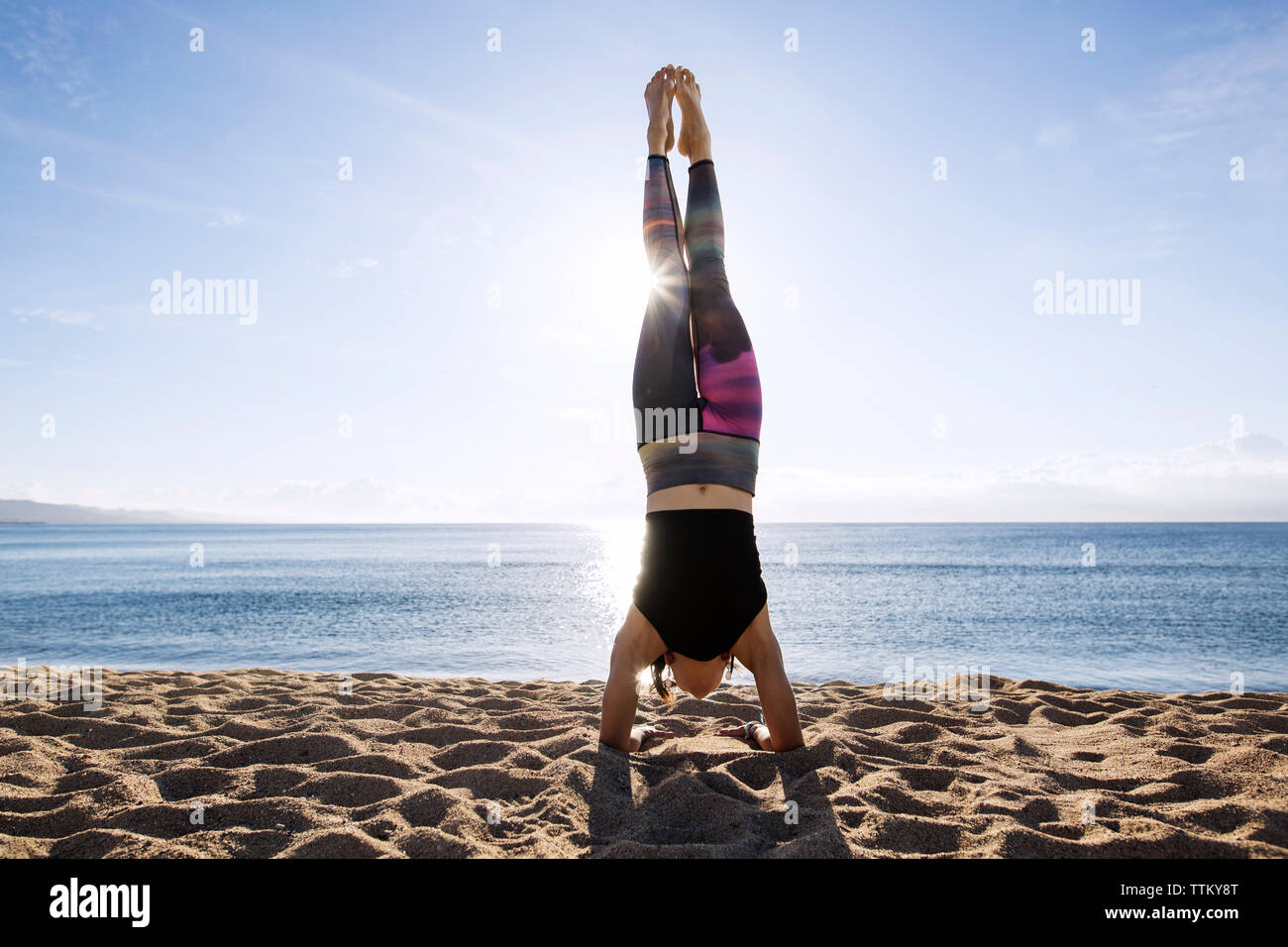 Junge Frau macht Handstand auf Ufer am Strand Stockfoto