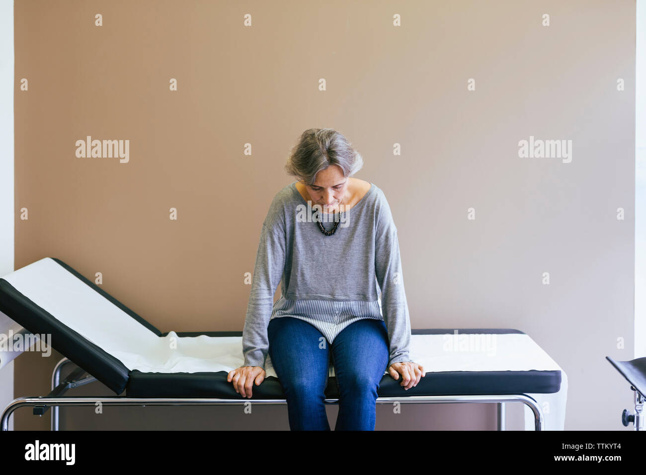 Ältere Patienten sitzen auf dem Bett gegen die Wand im Krankenhaus Stockfoto