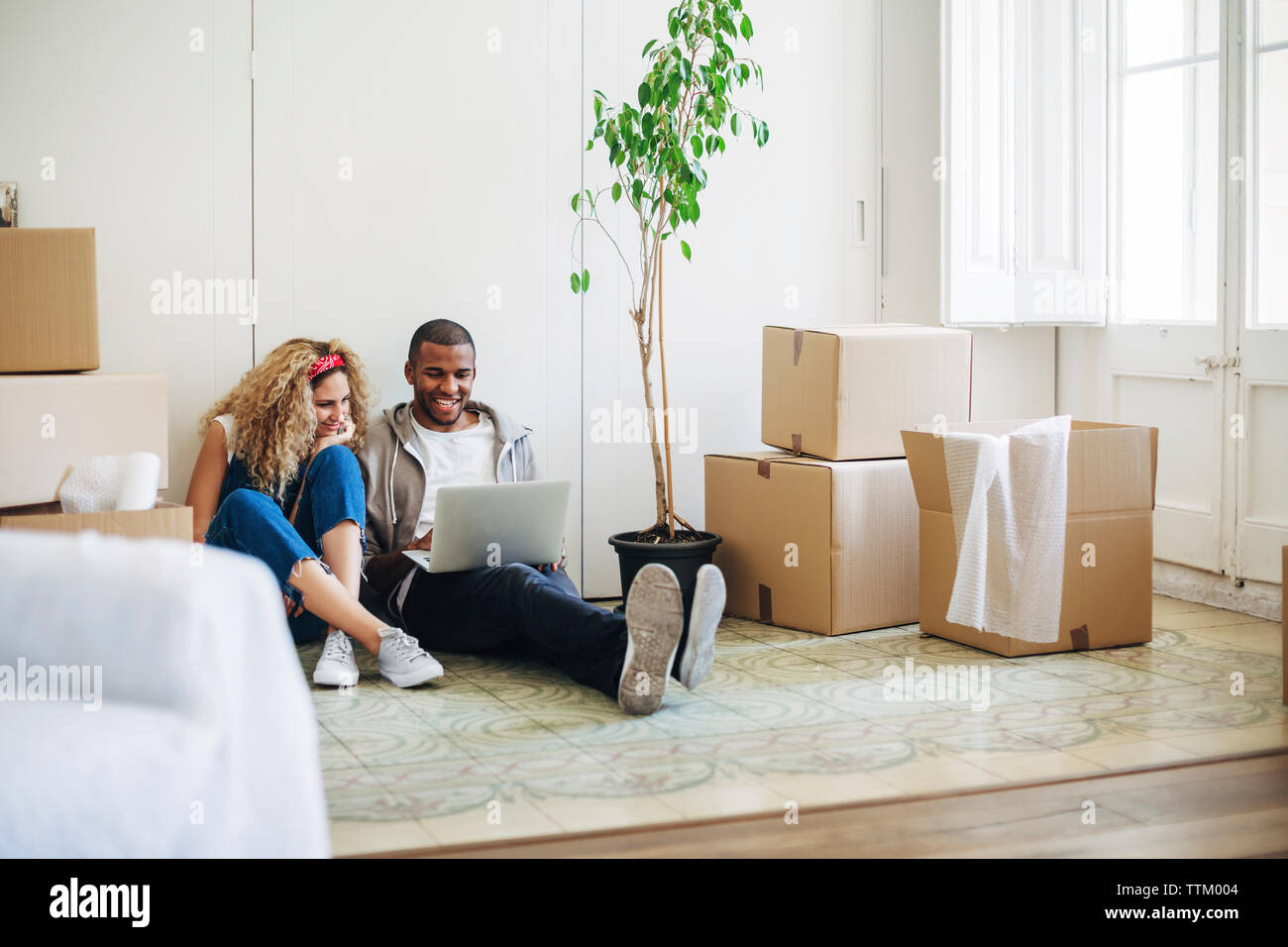 Lächelndes Paar mit Laptop Computer, während auf dem Boden am neuen Haus sitzt Stockfoto