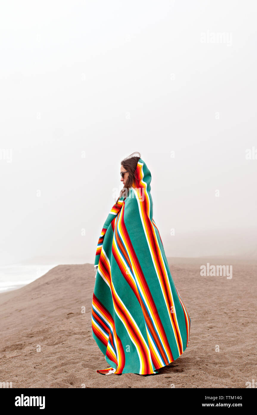 Seitenansicht der Frau in ein Handtuch eingewickelt stehend auf Sand gegen den klaren Himmel Stockfoto