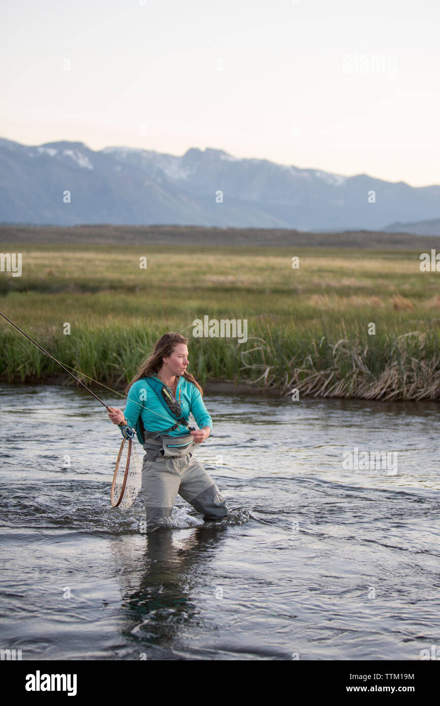 Junge Frau Fliegenfischen beim Stehen in Owens River gegen Berge Stockfoto
