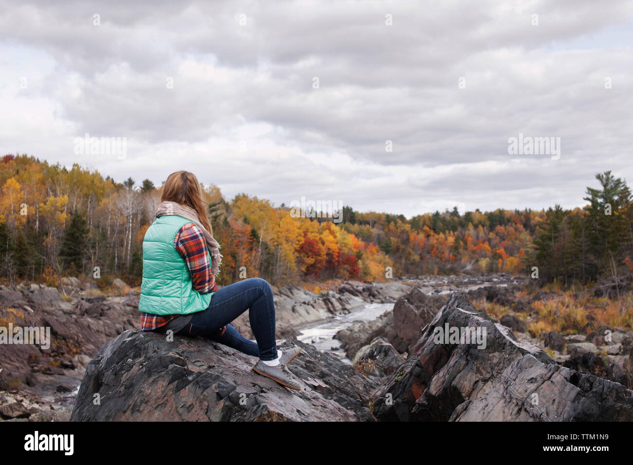 Frau sitzt auf Felsen an Jay Cooke State Park gegen bewölkter Himmel Stockfoto