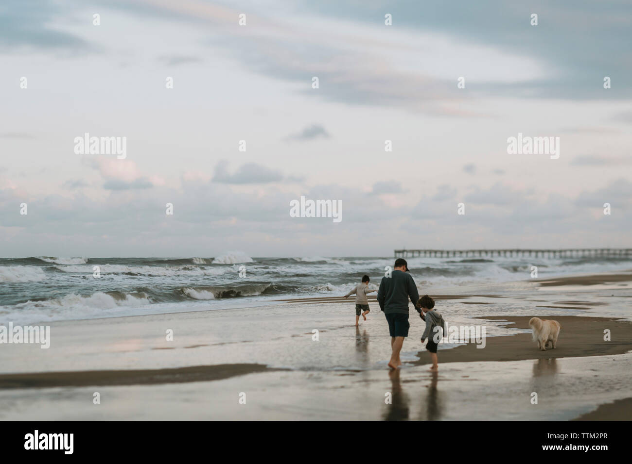 Familie mit Hund genießen am Strand gegen bewölkter Himmel bei Sonnenuntergang Stockfoto