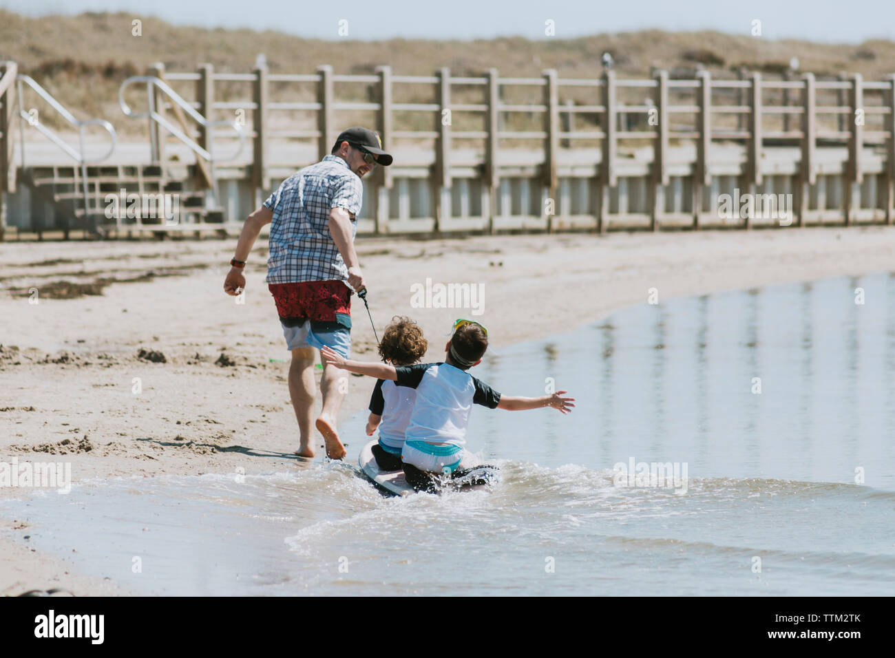 Ruckansicht Der Gluckliche Vater Ziehen Kinder Sitzen Auf Surfbrett Im Meer Wahrend Der Sonnigen Stockfotografie Alamy