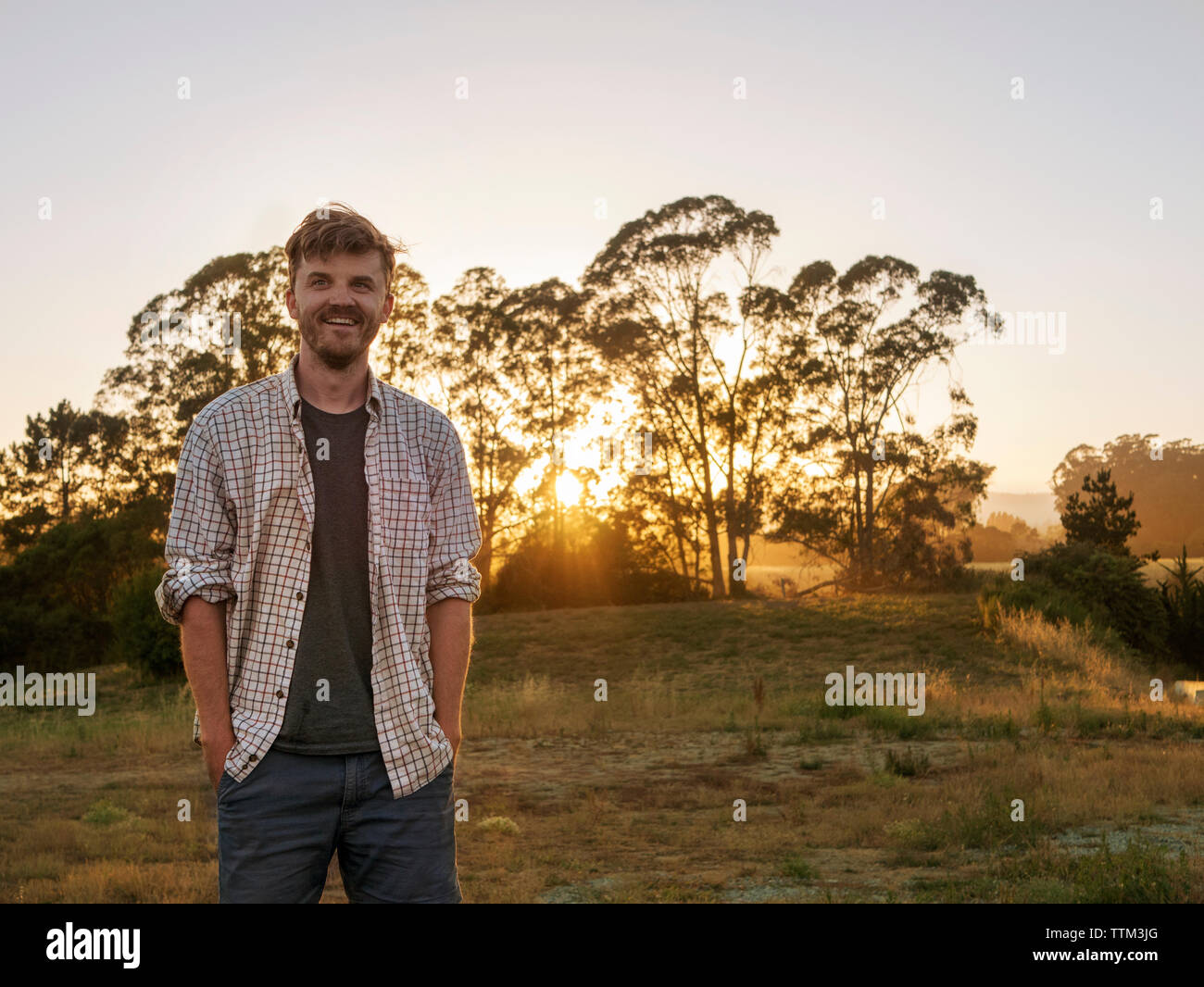 Glücklich Mann stand mit den Händen in den Taschen auf dem Feld bei Sonnenuntergang Stockfoto