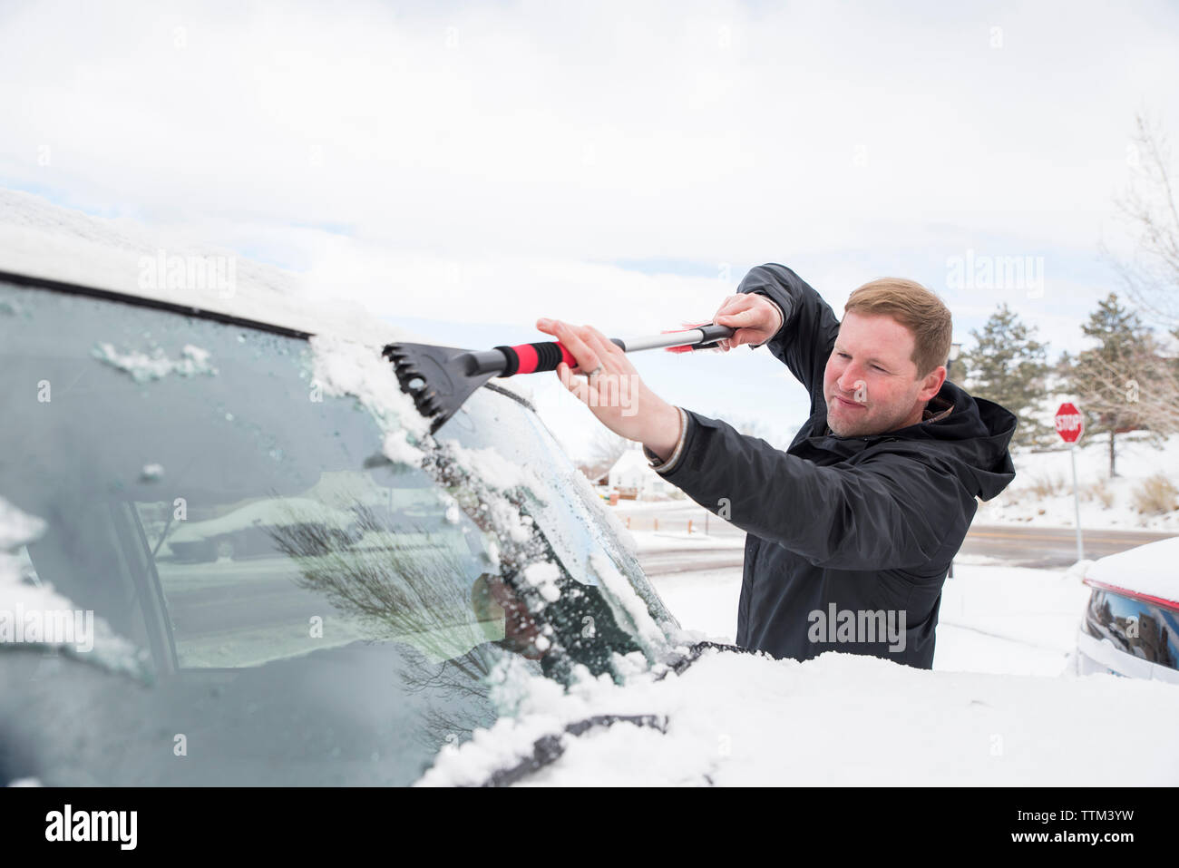 Mann, der schnee und eis von der windschutzscheibe des autos mit einer  bürste putzt person, die im winter frischen schnee nach einem schneesturm  vom auto putzt schneeschicht auf der windschutzscheibe des fahrzeugs