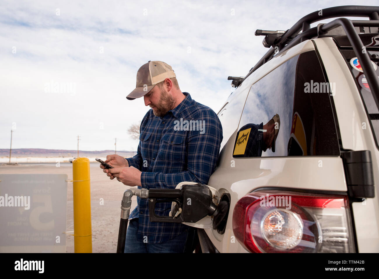 Mitte der erwachsene Mann mit Smart Phone, während mit dem Auto an der Tankstelle stehen Stockfoto
