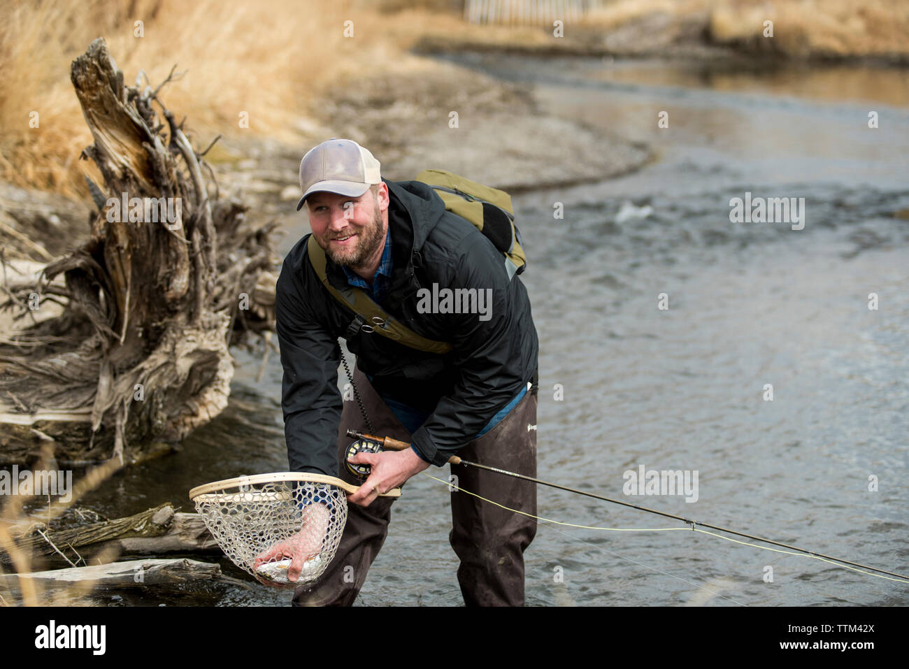 Lächelnd Mann entfernen Fisch von Butterfly Fischernetz während in Fluß Stockfoto