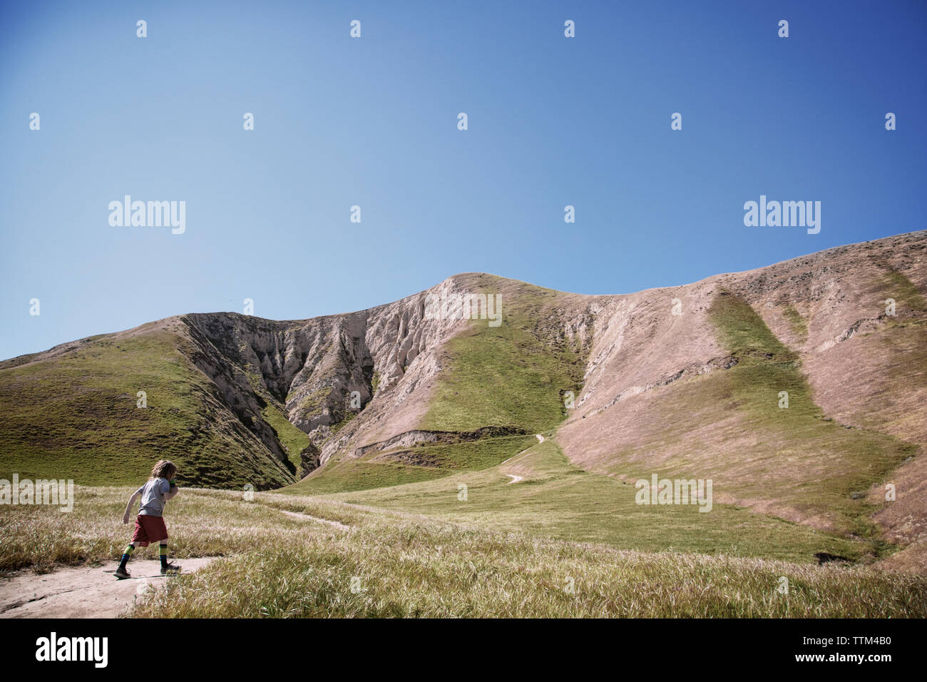 Junge Wandern auf Trail im Feld von Bergen gegen den klaren blauen Himmel Stockfoto