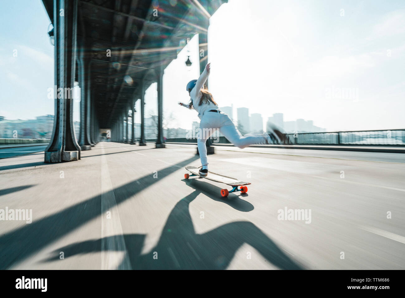 Verschwommene Bewegung von Frau skateboarding unter Brücke in der Stadt gegen den Himmel Stockfoto